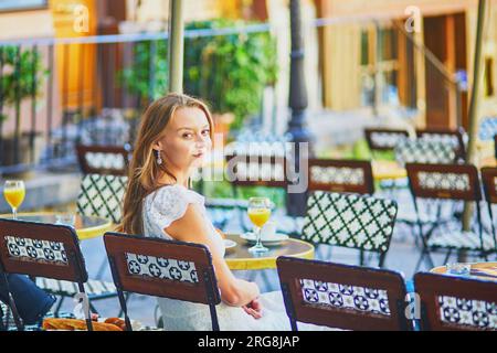 Jeune femme joyeuse prenant le petit déjeuner ou brunch dans un café français traditionnel sur Montmartre à Paris, France Banque D'Images