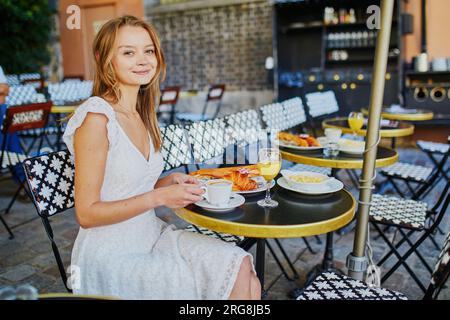 Jeune femme joyeuse prenant le petit déjeuner ou brunch dans un café français traditionnel sur Montmartre à Paris, France Banque D'Images