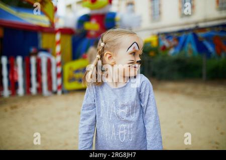 Petite fille d'enfant d'âge préscolaire avec la peinture de visage de chat, faisant grimace drôle à l'extérieur. Peinture de visage d'enfants. Activités créatives pour les enfants Banque D'Images