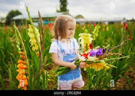 Adorable fille cueillant de belles fleurs de gladiolus à la ferme. Activités estivales en plein air pour les petits enfants. Banque D'Images