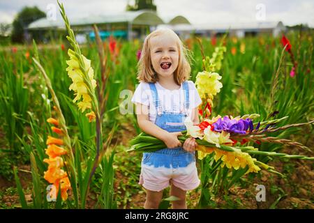 Adorable fille cueillant de belles fleurs de gladiolus à la ferme. Activités estivales en plein air pour les petits enfants. Banque D'Images