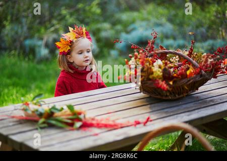 Beau portrait d'automne d'adorable fille d'enfant d'âge préscolaire dans la couronne colorée de feuilles d'érable sur sa tête. Enfant regardant la décoration d'automne pour la table Banque D'Images