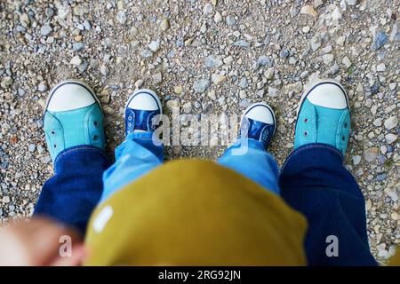 Closeupe de jambes d'un adulte et d'un tout-petit en jeans et baskets. Mère et fille s'amusant ensemble à l'extérieur. Parent aidant l'enfant à faire les premiers s Banque D'Images