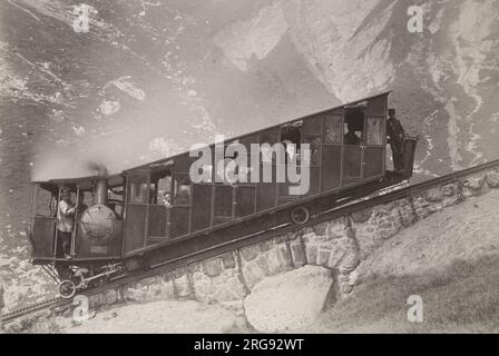 Un wagon de chemin de fer suisse à crémaillère et pignon à voie étroite, construit vers 1900, avec des conducteurs et des passagers, sur une voie en pente raide dans les Alpes. D'après les archives de Gloucester Coach and Wagon Works au Gloucester Record Office. Banque D'Images