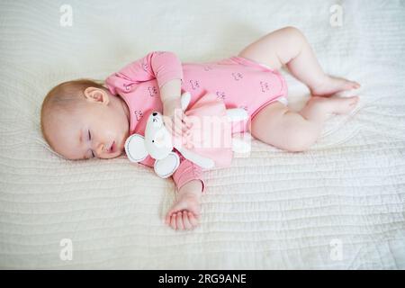 Bébé fille ayant une sieste avec son jouet de souris préféré. Petit enfant dormant sur le lit avec couette. Concept d'entraînement au sommeil. Enfant en bas âge dans la crèche ensoleillée Banque D'Images