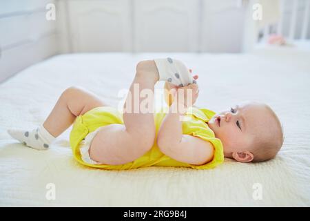 Adorable petite fille enlevant la chaussette de son pied. Petit enfant s'amusant. Enfant en bas âge dans la crèche ensoleillée Banque D'Images