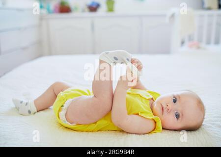 Adorable petite fille enlevant la chaussette de son pied. Petit enfant s'amusant. Enfant en bas âge dans la crèche ensoleillée Banque D'Images