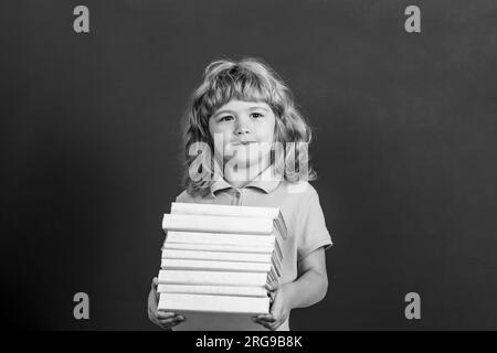 Concept d'éducation et de créativité. Enfant tenant la pile de livres avec le panneau de mortier sur le tableau noir. Retour à l'école. Écolier en classe. Noir et blanc Banque D'Images