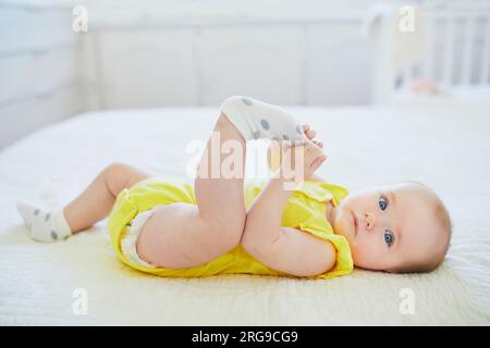 Adorable petite fille enlevant la chaussette de son pied. Petit enfant s'amusant. Enfant en bas âge dans la crèche ensoleillée Banque D'Images