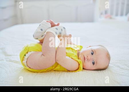 Adorable petite fille enlevant la chaussette de son pied. Petit enfant s'amusant. Enfant en bas âge dans la crèche ensoleillée Banque D'Images