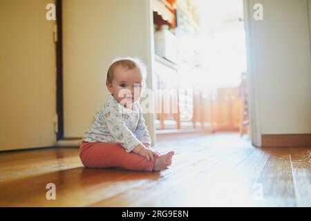 Petite fille assise sur le sol à la maison. Petit enfant rampant à la maison et explorant la chambre Banque D'Images