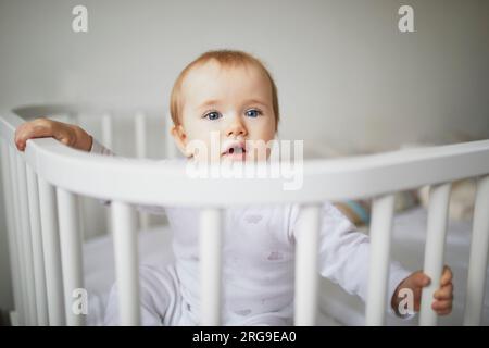 Adorable petite fille dans le lit de lit co-couchette attaché au lit des parents. Petit enfant assis dans un lit Banque D'Images