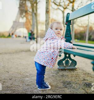 Une fille d'un an debout à côté du banc près de la tour Eiffel. Tout-petit apprenant à marcher. Adorable enfant marchant à Paris, France. Voyager avec Banque D'Images