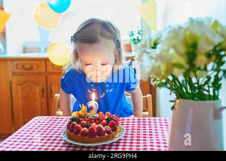 Heureuse petite fille en robe bleue célébrant son deuxième anniversaire. Petit enfant avec gâteau d'anniversaire et bougie Banque D'Images