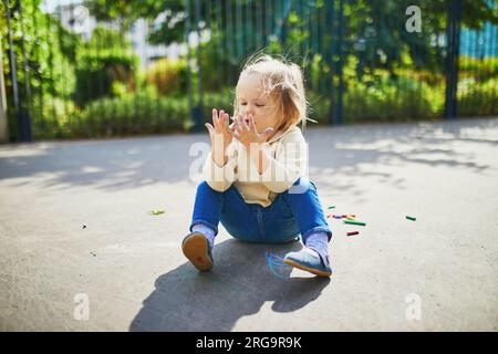 Adorable petite fille à ses mains sales après avoir dessiné avec des craies colorées sur l'asphalte. Activités de plein air et jeux créatifs pour les petits enfants Banque D'Images