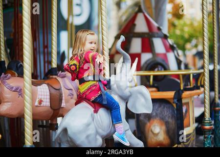 Enfant en bas âge s'amusant sur le manège français vintage à Paris, France. Adorable petite fille sur le terrain de jeu. Activités de plein air pour les petits enfants Banque D'Images