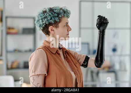 Portrait de vue latérale de jeune femme regardant le bras prothétique cyber et souriant Banque D'Images