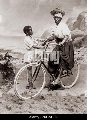 C.1900 Antilles - vieille femme sur un vélo avec un enfant maintenant. Portrait de studio. Banque D'Images