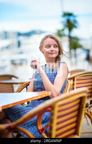 Jeune française buvant du vin rouge dans un café en plein air de Cannes Banque D'Images