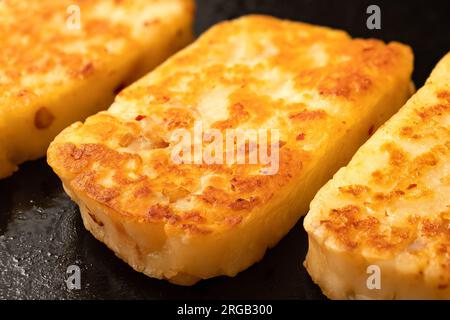 Détail des tranches frites de fromage halloumi avec du piment rouge sur une poêle noire. Banque D'Images