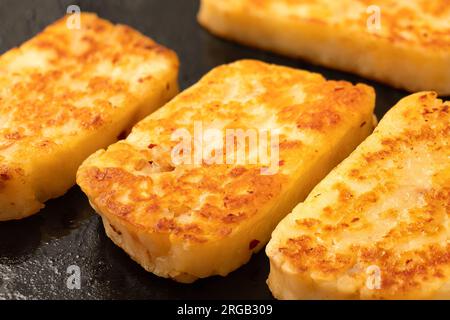 Détail des tranches frites de fromage halloumi avec du piment rouge sur une poêle noire. Banque D'Images