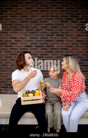 Famille avec une mère, un père et une fille assis à l'extérieur sur les marches d'un porche avant d'une maison en brique Banque D'Images