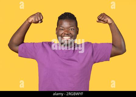 Fort African American Guy montrant les muscles de biceps sur fond jaune Banque D'Images