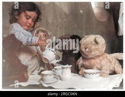 Une petite fille accueille une fête de thé - trois ours et une poupée assistent. Banque D'Images