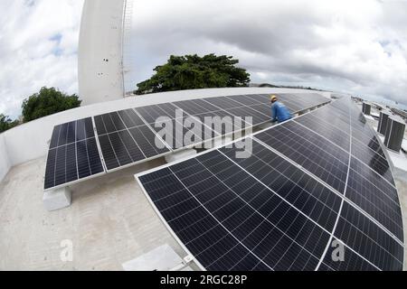 salvador, bahia, brésil - 17 juillet 2023 : un ouvrier installe des panneaux solaires sur le toit d'une école publique de la ville de Salvador. Banque D'Images