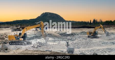 Excavatrices plaçant des pierres dans une excavation au coucher du soleil avec une montagne en arrière-plan Banque D'Images