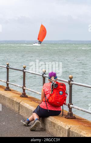 jeune femme assise sur le mur de la mer au bord de la mer à cowes sur l'île de wight regardant la cowes week régate yachts course. Banque D'Images