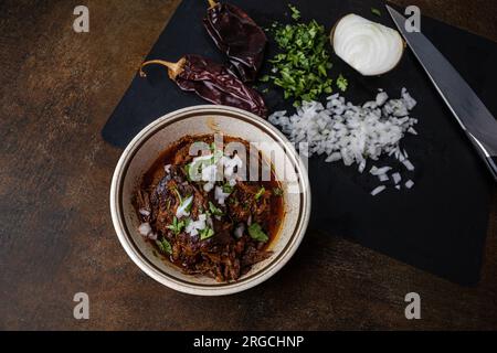 Un bol de viande de bœuf bigria cuite lentement et braisée dans un bol d'époque avec des oignons hachés, de la coriandre, des poivrons guajillo et du bouillon Banque D'Images