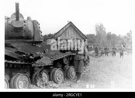 Un char lourd soviétique 'KV-1 Shielded', renversé par un incendie anti-char allemand, avec des dommages indiqués par un soldat allemand envahissant. Le 'KV-1 Shielded' était un kV-1 standard avec une armure supplémentaire rivée sur la tourelle et les parties de la coque. L'armure supplémentaire est visible sur le côté de la tourelle. (Les chars Kliment Voroshilov (KV) sont une série de chars lourds soviétiques nommés d'après le commissaire de la défense soviétique et le politicien Kliment Voroshilov) Banque D'Images