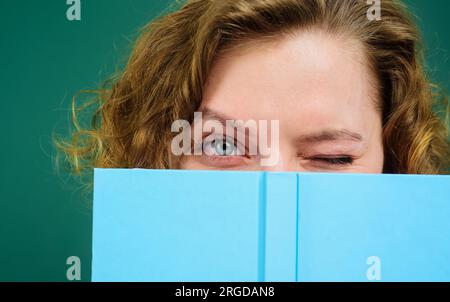 Gros plan portrait d'un enseignant clignant avec un bloc-notes. Fournitures scolaires. Retour à l'école. Étudiante se cachant derrière un livre ouvert. Fille couvre le visage Banque D'Images