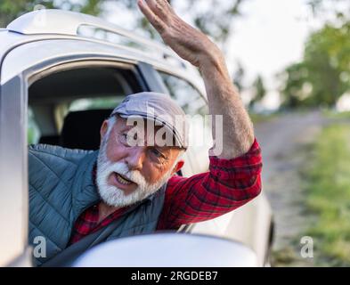 Homme senior conduisant une voiture, regardant par la fenêtre et se disputant avec quelqu'un Banque D'Images