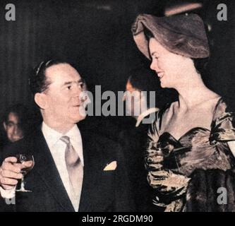 La créatrice de mode suisse britannique JO (Guiseppe) Mattli (1907-1982), photographiée parlant à la beaucoup plus grande Mme Rosemary Parker (une mannequin ?) Lors d'une réception pour les acheteurs de mode d'outre-mer tenue à la Mansion House dans la ville de Londres en 1955. La réception a été donnée par Lady Pamela Berry (anciennement Lady Pamela Smith) et a été suivie par les principaux designers de Londres, acheteurs étrangers, représentants de la presse, le président de la Chambre de commerce, M. Peter Thorneycroft et son épouse et la duchesse de Gloucester. Banque D'Images