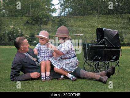 Un homme avec deux petits enfants - un garçon et une fille - et un bébé jouet dans un jardin bien entretenu. Banque D'Images