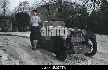 Une jeune femme debout près d'une voiture à toit ouvert par temps froid avec une pluie de neige sur le sol. Banque D'Images