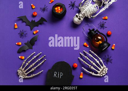Composition avec des cors de bonbons savoureux, squelette, lanterne et décor d'Halloween sur fond violet Banque D'Images