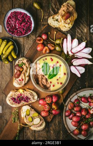 Pâté étalé dans un bocal en verre sur une planche de bois avec raisins grillés, radis, cornichons et baguette Banque D'Images