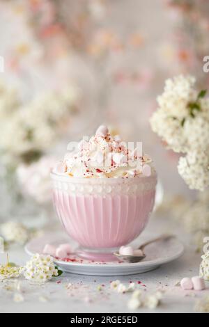 Une tasse en verre avec une boisson au chocolat chaud rose garnie de crème fouettée et de mini guimauves. Banque D'Images