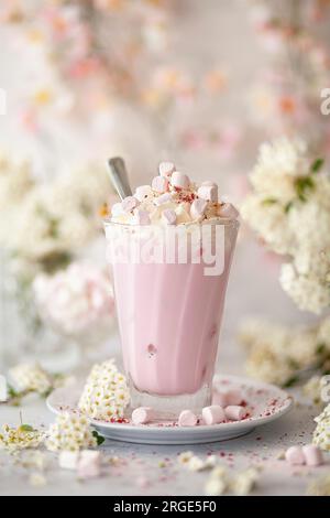 Une boisson au chocolat chaud rose servie sur de la glace et garnie de crème fouettée et de guimauves. Banque D'Images