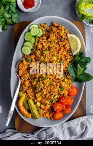 Salade de boulgour turque garnie de tomates tranchées et concombres, de feuilles de menthe fraîche, de cornichons et de citron dans une assiette ovale. Banque D'Images