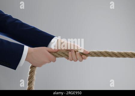 Concept de litige. Homme d'affaires tirant la corde sur fond gris clair, closeup Banque D'Images