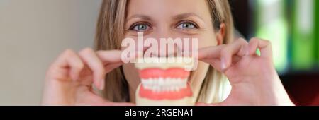 Dentiste tient des mâchoires en plastique avec des dents artificielles devant sa bouche. Banque D'Images