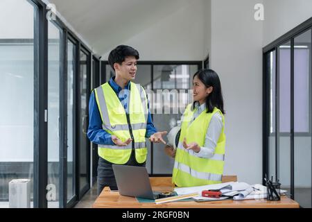 Deux jeunes hommes et femmes ingénieurs se réunissent, travaillent, discutent, planifient, conçoivent, mesure de la disposition des plans de construction dans le plancher du chantier Banque D'Images