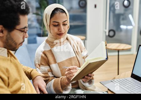 Portrait de jeune femme musulmane portant le foulard dans le bureau et parlant à un collègue masculin discutant des notes Banque D'Images