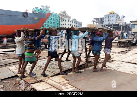 Dhaka, Dhaka, Bangladesh. 9 août 2023. Un groupe de porteurs transporte une lourde plaque d'acier de 250 kg dans un chantier naval sur la rive de la rivière Buriganga, à Keraniganj, près de Dhaka, Bangladesh. Des douzaines de chantiers navals occupant 30,96 acres de la côte de Buriganga sont en activité depuis 50 ans. Il est principalement utilisé pour la fixation et la réparation de vieux navires, et construire dans de nouveaux navires. Les travailleurs travaillent dans le chantier naval sans casques, masques faciaux ou chaussures de sécurité. Ils travaillent dur toute la journée, mais reçoivent toujours un salaire minimum. Avec un nombre croissant de commandes des acheteurs locaux et mondiaux, le shipbuil Banque D'Images