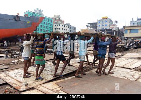 Dhaka, Dhaka, Bangladesh. 9 août 2023. Un groupe de porteurs transporte une lourde plaque d'acier de 250 kg dans un chantier naval sur la rive de la rivière Buriganga, à Keraniganj, près de Dhaka, Bangladesh. Des douzaines de chantiers navals occupant 30,96 acres de la côte de Buriganga sont en activité depuis 50 ans. Il est principalement utilisé pour la fixation et la réparation de vieux navires, et construire dans de nouveaux navires. Les travailleurs travaillent dans le chantier naval sans casques, masques faciaux ou chaussures de sécurité. Ils travaillent dur toute la journée, mais reçoivent toujours un salaire minimum. Avec un nombre croissant de commandes des acheteurs locaux et mondiaux, le shipbuil Banque D'Images