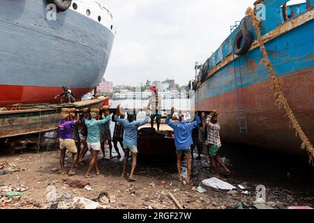 Dhaka, Dhaka, Bangladesh. 9 août 2023. Un groupe de porteurs transporte une lourde plaque d'acier de 250 kg dans un chantier naval sur la rive de la rivière Buriganga, à Keraniganj, près de Dhaka, Bangladesh. Des douzaines de chantiers navals occupant 30,96 acres de la côte de Buriganga sont en activité depuis 50 ans. Il est principalement utilisé pour la fixation et la réparation de vieux navires, et construire dans de nouveaux navires. Les travailleurs travaillent dans le chantier naval sans casques, masques faciaux ou chaussures de sécurité. Ils travaillent dur toute la journée, mais reçoivent toujours un salaire minimum. Avec un nombre croissant de commandes des acheteurs locaux et mondiaux, le shipbuil Banque D'Images